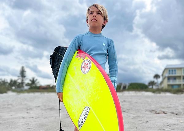 Photo of team rider Kai Peters holding surfboard at the beach