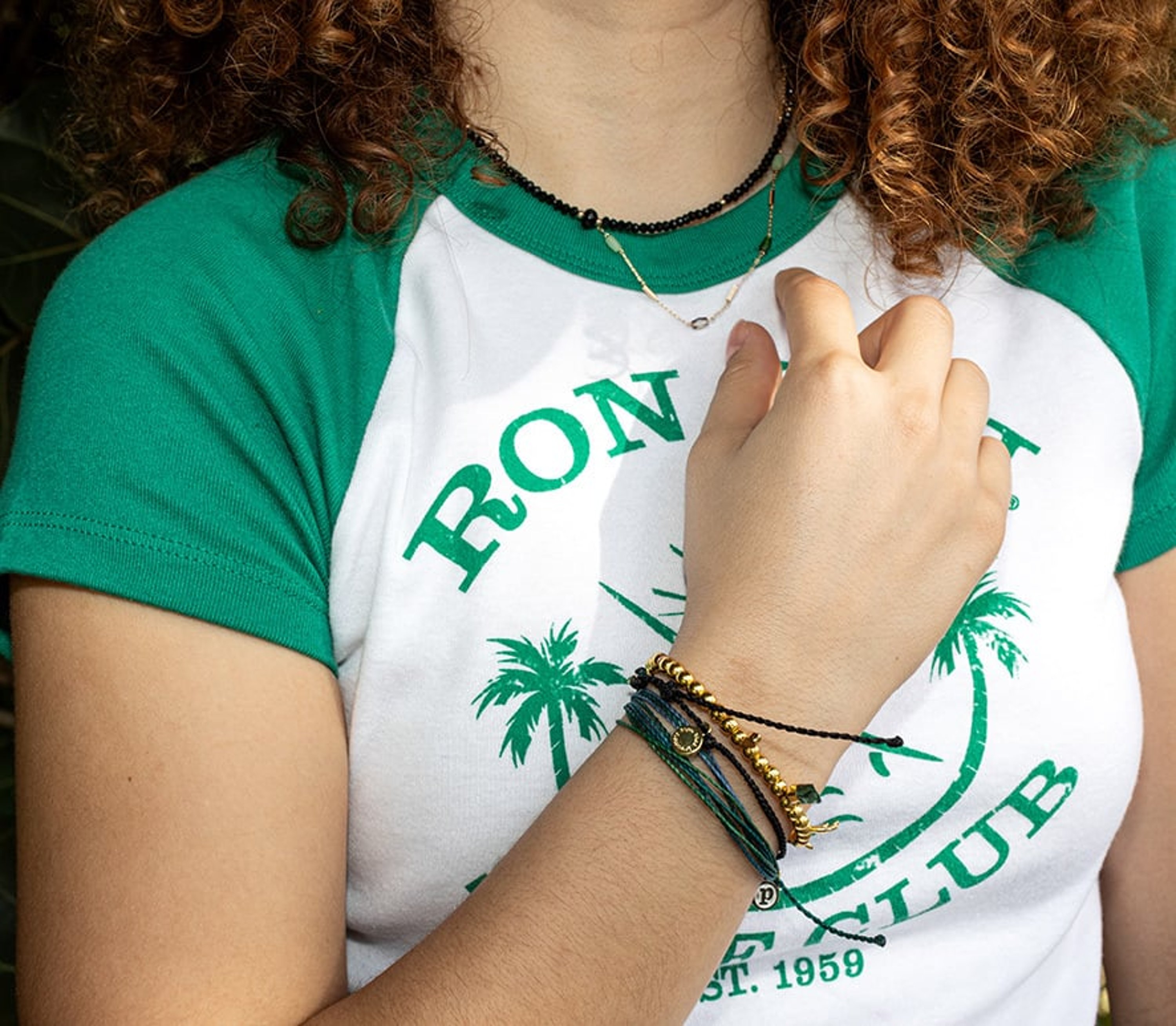 a girl in a Ron Jon tee, showing her bracelets and necklaces