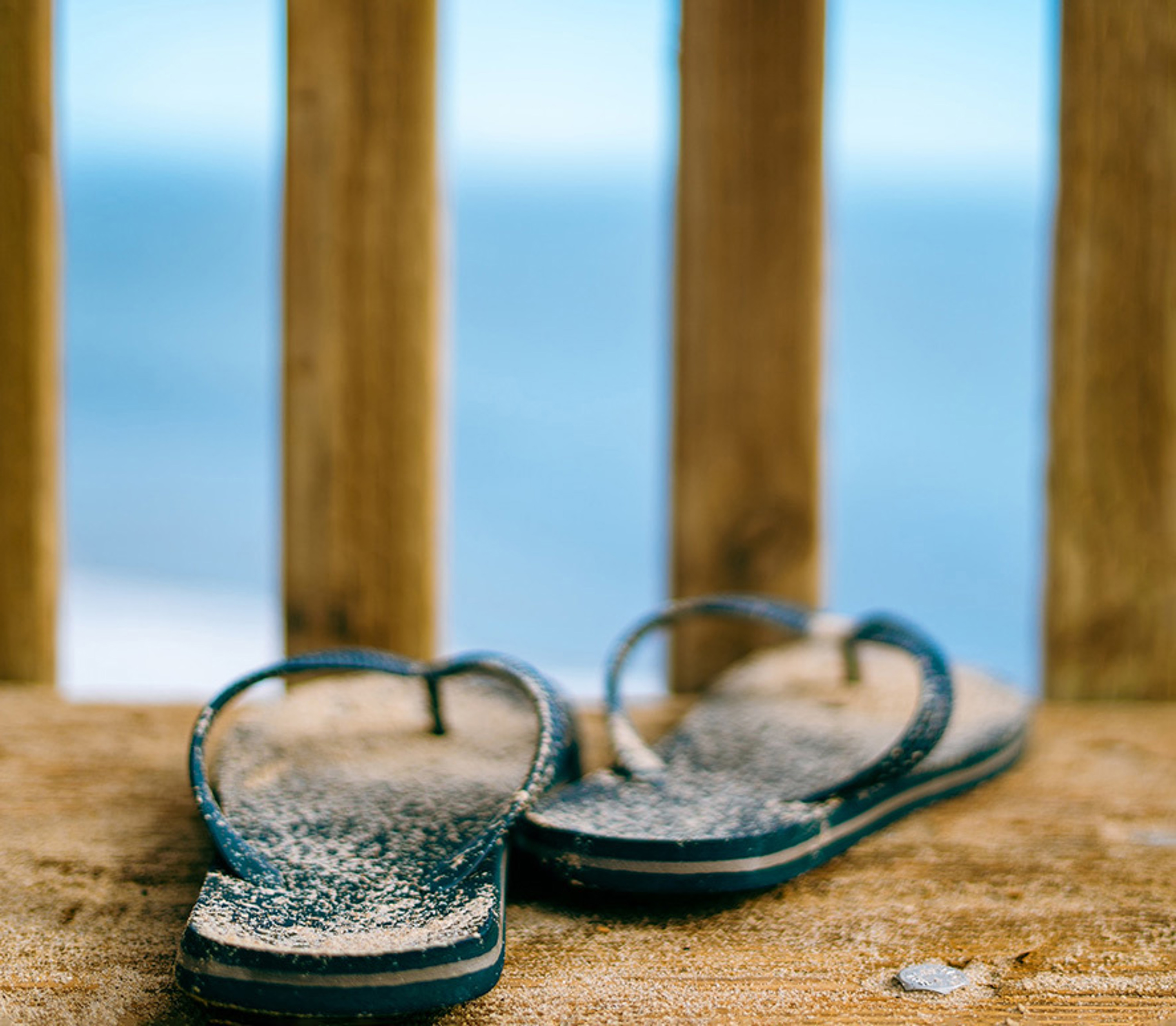 sand covered flip-flops on a deck over the water