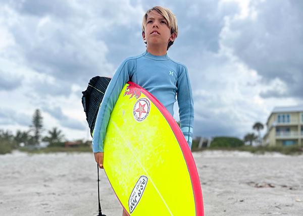 Photo of team rider Kai Peters holding surfboard at the beach