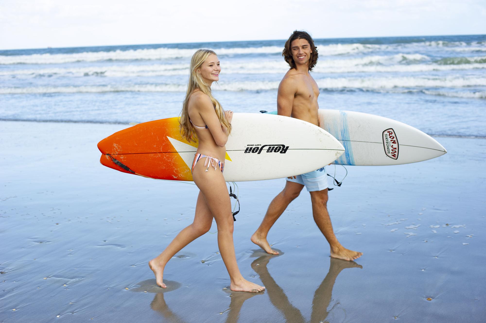 guy and girl walking with surfboards in front of the ocean
