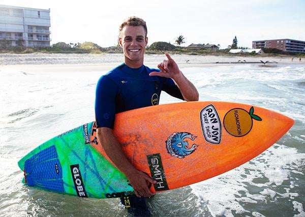 Photo of team rider Corey Howell holding surfboard in the ocean