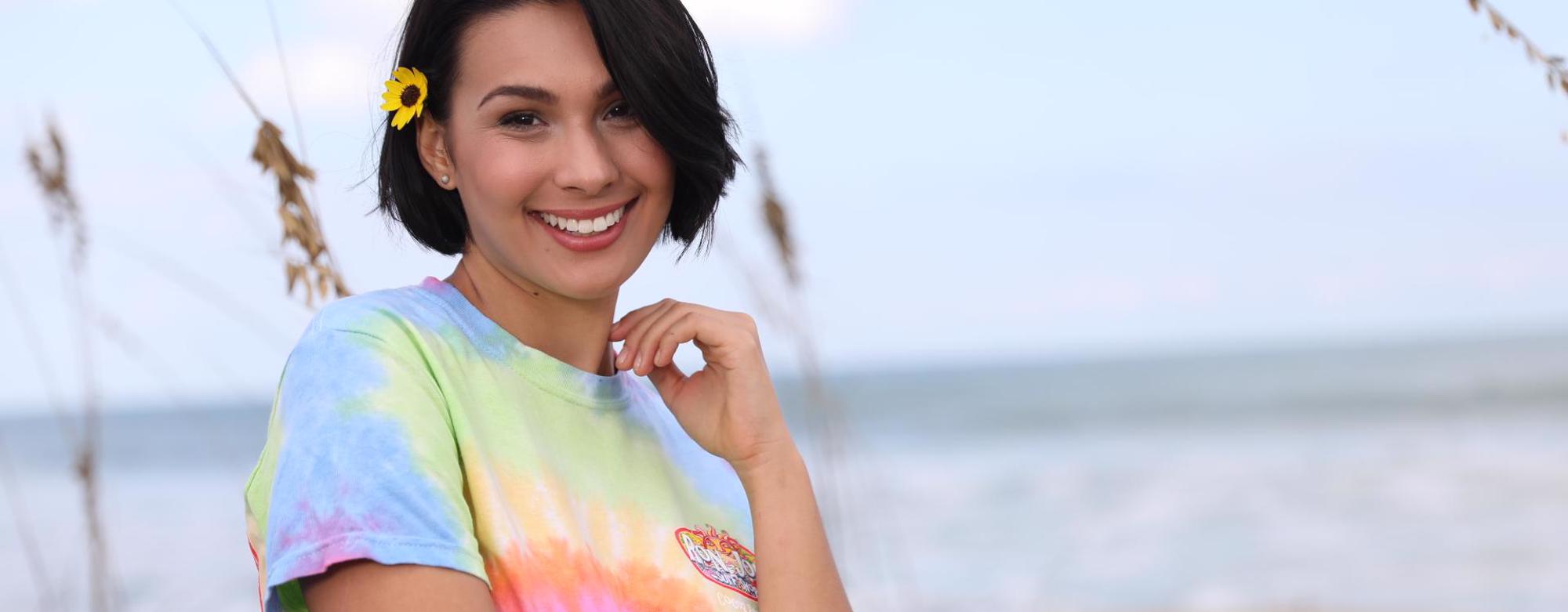 girl wearing tie-dye tee shirt with beach in background