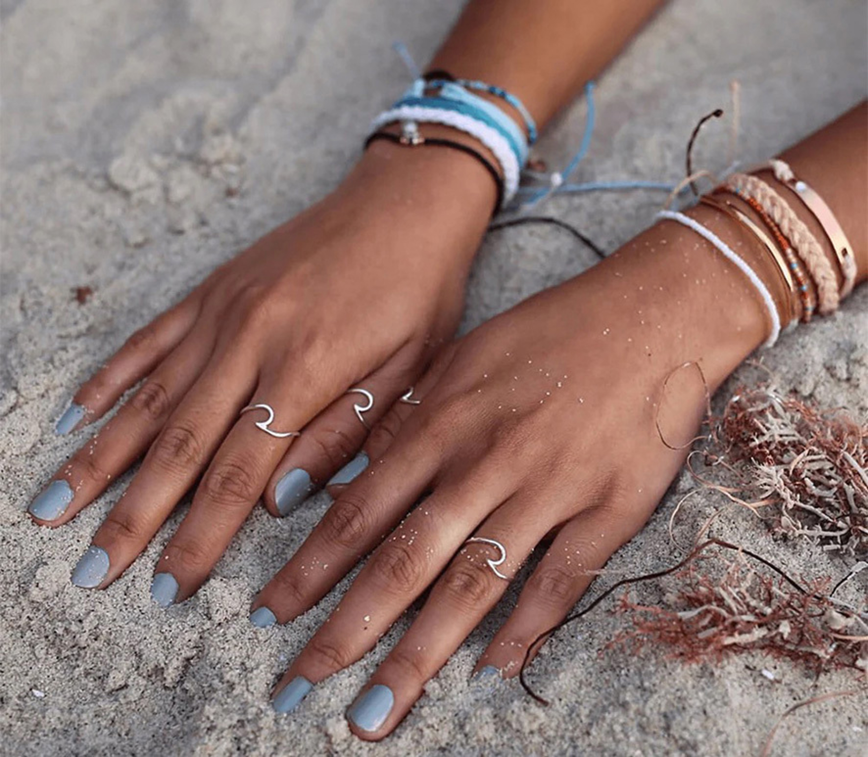 two hands on beach sand showing off thread bracelets and metal rings
