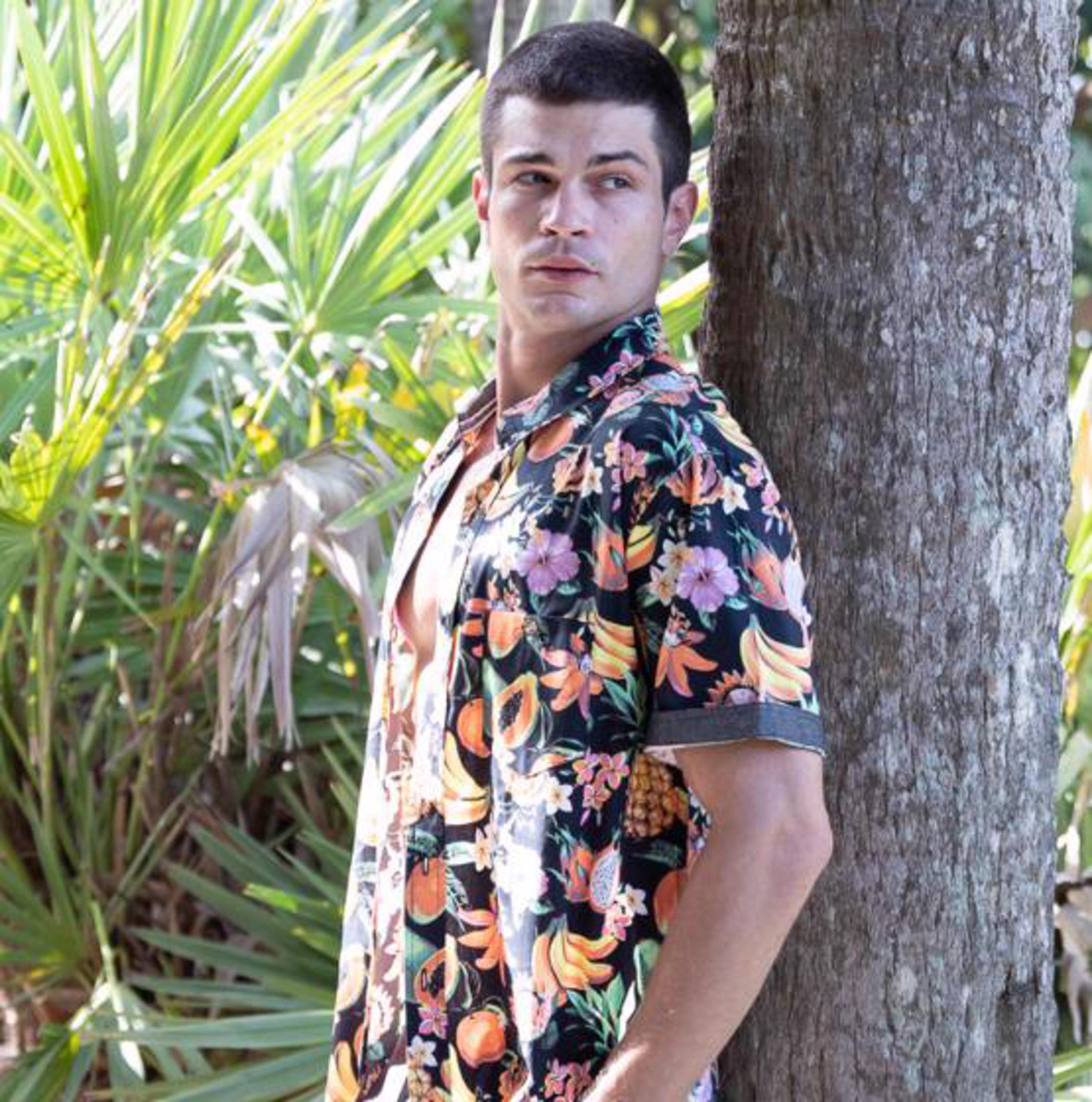 guy wearing button down shirt leaning against palm tree 