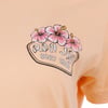 Peach-colored T-shirt with RON JON SURF SHOP and pink hibiscus flowers printed on the front.