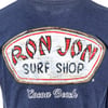 Close-up of a shirt with a weathered Ron Jon Surf Shop logo and Cocoa Beach text on a dark blue fabric.