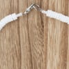Close-up of a white beaded necklace with a metal clasp, displayed on a light brown wooden surface.