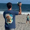 Man on beach holding a ball, with a child in the background. Ocean waves and clear sky in the distance.