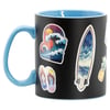 A black mug with a light blue handle features colorful stickers of a wave, a surfboard, flip-flops, a sunset, and a pineapple.