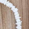 A strand of irregularly shaped white beads arranged in a curved line on a wooden surface.
