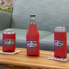 Three drinks‚Äîtwo cans and one bottle‚Äîeach in a red Ron Jon Surf Shop coozie, are placed on a wooden table in front of a blue-green couch.