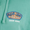 Close-up of a teal hoodie featuring the Ron Jon Surf Shop logo with Cocoa Beach text underneath.