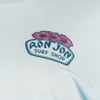 A close-up of a Ron Jon Surf Shop logo with three pink flowers above the text on a light blue fabric background.