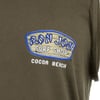 Close-up of a dark shirt featuring a Ron Jon Surf Shop Cocoa Beach logo in blue, white, and beige on the upper left chest area.