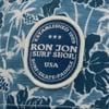 Close-up of a blue and white Hawaiian print fabric featuring an oval patch reading Established 1959, Ron Jon Surf Shop, USA, Surf, Skate, Paddle.