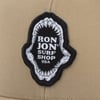 Beige fabric with a patch featuring a shark mouth design surrounding the text Ron Jon Surf Shop USA.