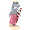 A cartoon shark figurine wearing sunglasses and a pink grass skirt, holding a striped surfboard labeled Ron Jon Surf Shop while standing on a sandy base with coral.