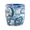 A ceramic mug with a blue interior, featuring a design of blue octopus tentacles wrapping around the outside against a cloudy background.