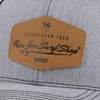 Close-up of a gray cap with a brown patch that reads, Established 1959, Ron Jon Surf Shop, featuring a small palm tree and wave design.