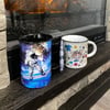 Two coffee mugs on a wooden ledge in front of a fireplace; one mug features an astronaut design, the other has colorful graphics and text.