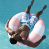 A man in floral swim shorts floats on a pink and white inflatable ring in a clear blue swimming pool.