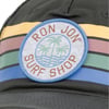 Cap with a Ron Jon Surf Shop patch featuring palm trees and waves, set against yellow, pink, green, and blue stripes.