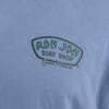 Light blue T-shirt featuring a RON JON SURF SHOP Cocoa Beach logo in green and black text.