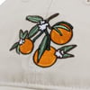 Embroidered design of oranges with green leaves and white flowers on a beige fabric.