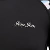 Close-up of a black garment showing the text Ron Jon in white, with colorful patterns partially visible at the edge.