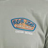 Green shirt with a Ron Jon Surf Shop, Cocoa Beach logo featuring blue lettering on a wooden sign design.