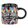 A black mug with colorful geometric patterns and the text Ron Jon Surf Shop printed on the front.