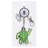 A keychain featuring a green cartoon turtle, a Ron Jon Surf Shop charm, and a round charm, attached to a metal keyring and clasp.