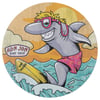 Cartoon shark wearing sunglasses and pink shorts surfing on a yellow board with Ron Jon Surf Shop logo in the background against an orange sky and ocean waves.