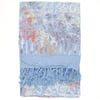 Light blue sarong with a colorful, abstract floral pattern and fringed tassels on one end, laid flat against a white background.