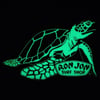 Glow-in-the-dark magnet of a sea turtle holding a sign that reads Ron Jon Surf Shop against a black background.