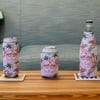 Three beverage containers‚Äîa tall can, standard can, and bottle‚Äîeach in Ron Jon Surf Shop tropical-patterned sleeves, are placed on coasters on a wooden table in front of a sofa.