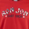 Red t-shirt with Ron Jon Surf Shop printed on it; Ron Jon letters are decorated with a stylized American flag pattern.