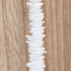 A vertical strand of irregularly shaped white beads is displayed against a light wood background.