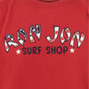 Red shirt with text Ron Jon Surf Shop in stylized letters decorated with an American flag pattern.
