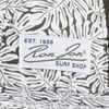Close-up of a fabric label with Ron Jon Surf Shop Est. 1959 text on a leaf-patterned background.