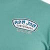 Close-up of a green shirt featuring a Ron Jon Surfboards Cocoa Beach, Fla. logo on the left chest area.