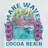 Colorful illustration of a woman surfing a wave with hibiscus flowers, a bird, and MAKE WAVES COCOA BEACH and Ron Jon Surf Shop text.