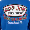 Back of a blue shirt featuring the Ron Jon Surf Shop logo with the phrases “One of a Kind” and “Cocoa Beach, Fla.” printed in red, white, and black.