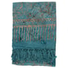 A teal and gold patterned sarong with fringe tassels along one edge, featuring abstract and geometric designs.