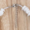 A close-up of a necklace clasp with a metal chain extender, white beads, and shell-like pieces on a wooden surface.