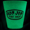 A glow-in-the-dark cup with the Ron Jon Surf Shop logo printed on it, shown in a dark setting.