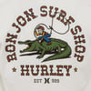 Cartoon cowboy riding an alligator inside a circular text reading Ron Jon Surf Shop Hurley on a white background.