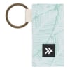 A rectangular fabric keychain with a brass-colored ring and a subtle green leaf pattern; a small black logo patch is attached.