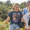 A smiling woman in a Ron Jon t-shirt holds a black soccer ball while walking outdoors with two other people.